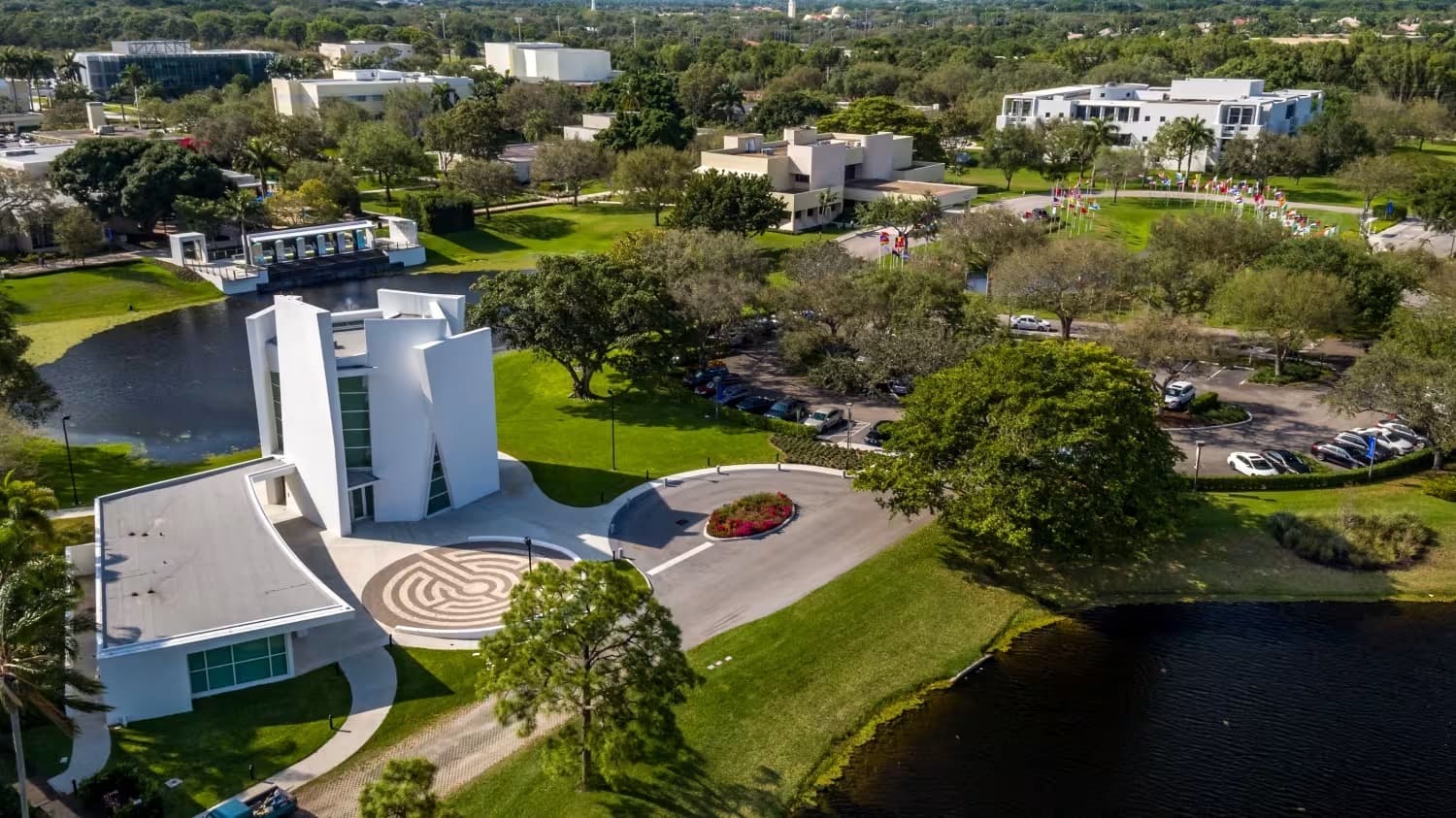Aerial view of the Lynn University campus in Boca Raton, showing the white sculptural chapel and its labyrinth beside the lake.